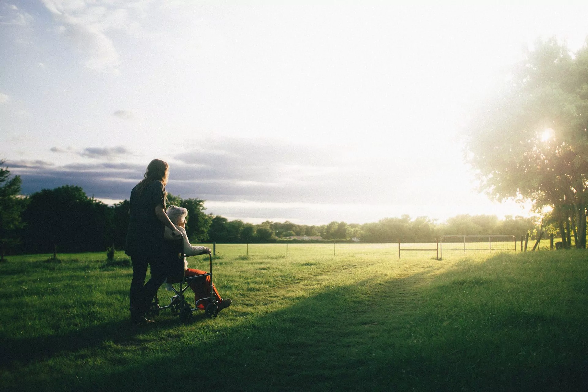 Woman pushing a senior woman in a wheelchair outside in the grass